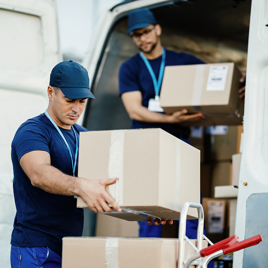 Young delivery man and his coworker unloading boxes from a van.